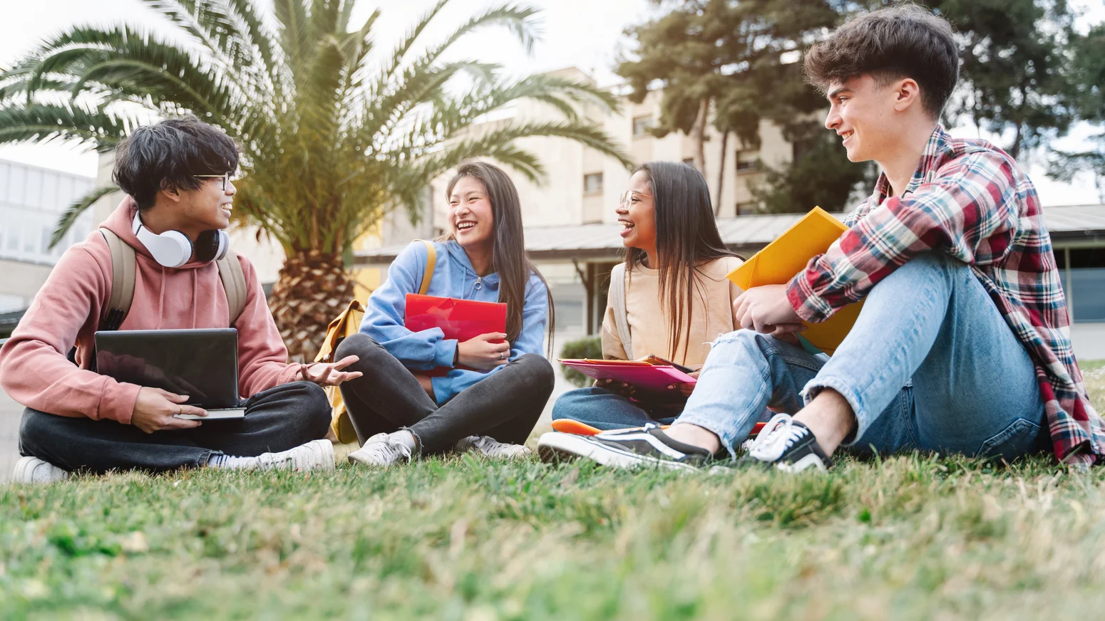 Eine Gruppe internationaler Austauschstudenten sitzt auf dem Rasen des Universitätsgeländes.