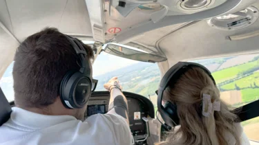 Im Cockpit eines Kleinflugzeugs zeigt der Pilot einer Studentin einen Punkt am Horizont beim Rundflug über die Stadt Worms.