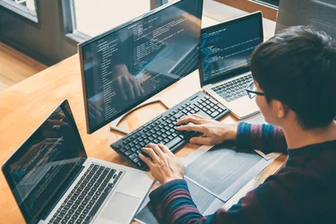 Anwendungsentwickler programmiert an mehreren Bildschirmen mit geöffnetem Quellcode.