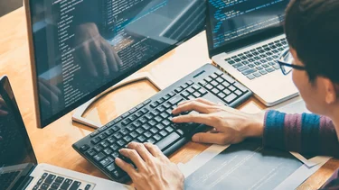 Anwendungsentwickler programmiert an mehreren Bildschirmen mit geöffnetem Quellcode.