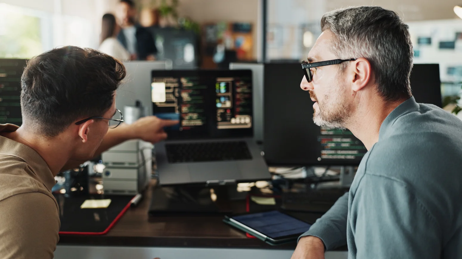 Zwei Personen besprechen Software und Programmcode an einem Arbeitsplatz.