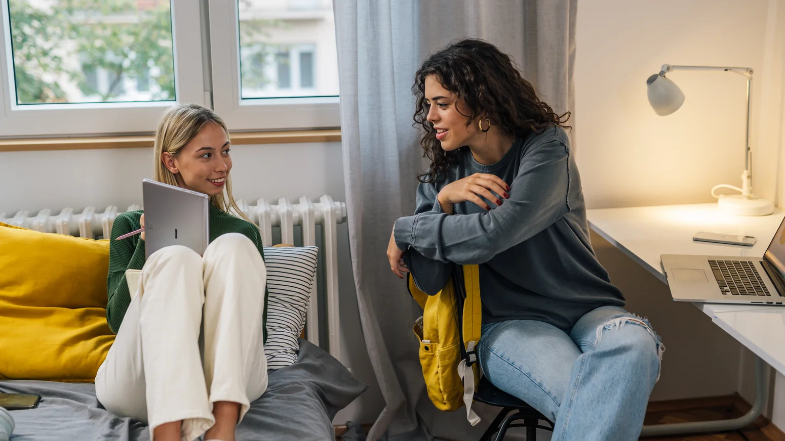Zwei Studentinnen, die im Zimmer auf dem Bett sitzen und sich unterhalten.