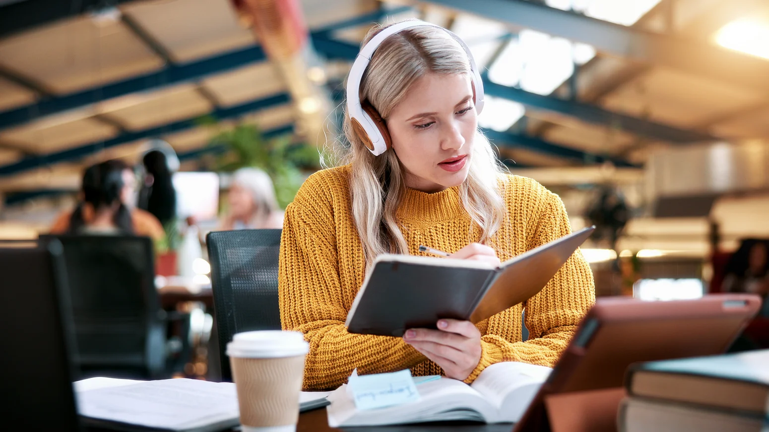 Studentin lernt mit Buch, Tablet und Kopfhörern in einer modernen Bibliotheksumgebung.