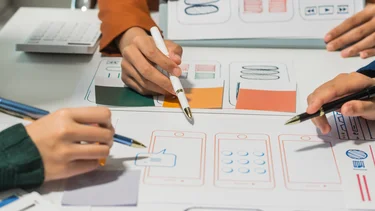 Mehrere Personen besprechen Wireframes und UI-Entwürfe für eine digitale Anwendung.