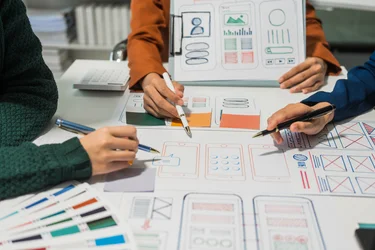 Mehrere Personen besprechen Wireframes und UI-Entwürfe für eine digitale Anwendung.