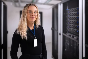 Systemadministratorin steht in einem Serverraum neben mehreren Server-Racks.