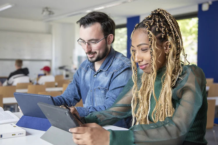Zwei Studierende arbeiten an ihren Tablets in einem Vorlesungsraum.
